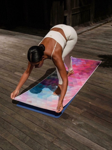 A high-quality lifestyle shot featuring a model using a geometric-patterned yoga mat on a rustic wooden deck.
